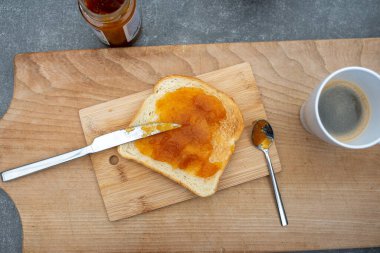 Bir tost ekmek ve kayısı reçeli ve tahtanın üzerinde bir fincan kahve..