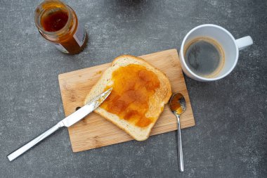 Bir tost ekmek ve kayısı reçeli ve tahtanın üzerinde bir fincan kahve..