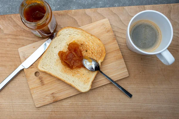 Bir tost ekmek ve kayısı reçeli ve tahtanın üzerinde bir fincan kahve..