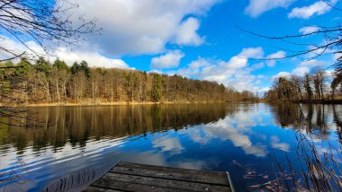 White clouds, blue sky and forest are reflected in the water
