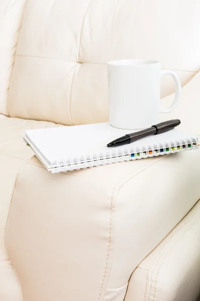 Coffee cup, pen, notebook is on white sofa — Stock Photo, Image