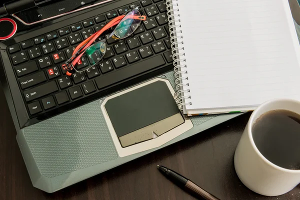 Taza de café, laptop, bolígrafo, bloc de notas y vasos en mesa de madera —  Fotos de Stock