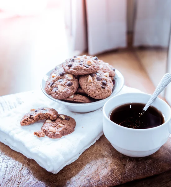 Galletas de chispas de chocolate en servilleta y té caliente en mesa de madera . — Foto de Stock