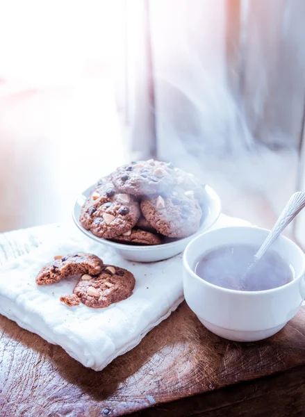 Galletas de chispas de chocolate en servilleta y té caliente en mesa de madera . — Foto de Stock