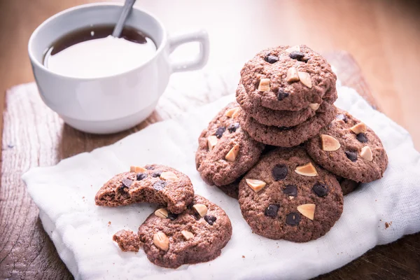 Biscoitos de chocolate em guardanapo e chá quente na mesa de madeira . — Fotografia de Stock