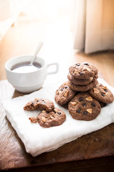 Galletas de chispas de chocolate en servilleta y té caliente en mesa de madera . —  Fotos de Stock