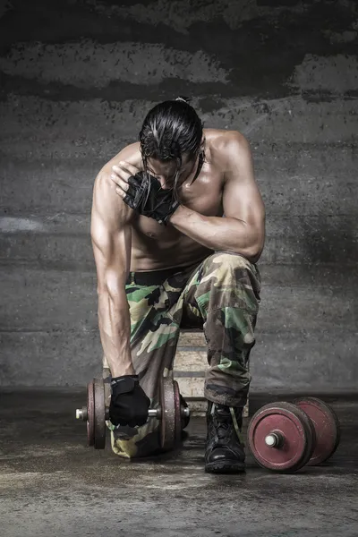 Otot atlet dengan celana kamuflase angkat besi di latar belakang dinding — Stok Foto