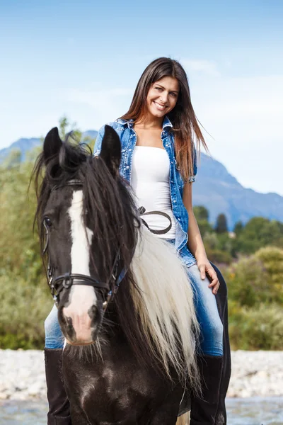 Young girl sitting on horse while crossing river in a mountainou — Stock Photo, Image