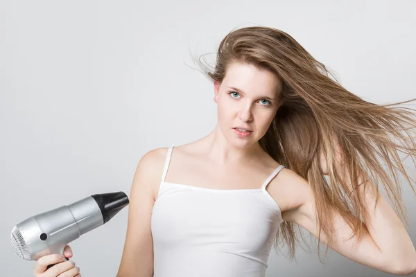 Attraente ragazza soffiare asciugandosi i capelli e guardando la fotocamera — Foto Stock