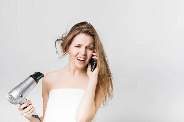 Beautiful young girl blow drying her hair while talking on the s — Stock Photo, Image