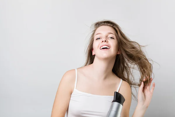 Beautiful teenager blow drying her hair and looking at camera — Stock Photo, Image