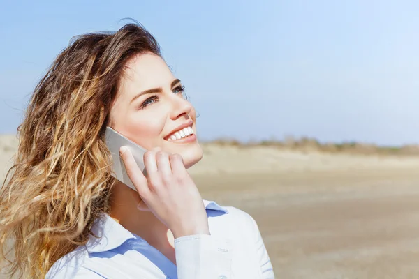 Mujer feliz sonriendo en el teléfono móvil en la playa —  Fotos de Stock