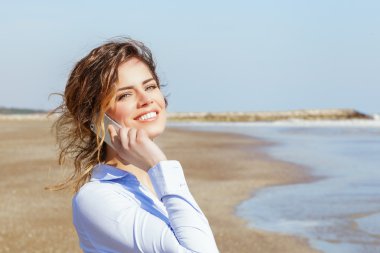 Deniz kenarında cep telefonunda gülümseyen güzel genç kadın