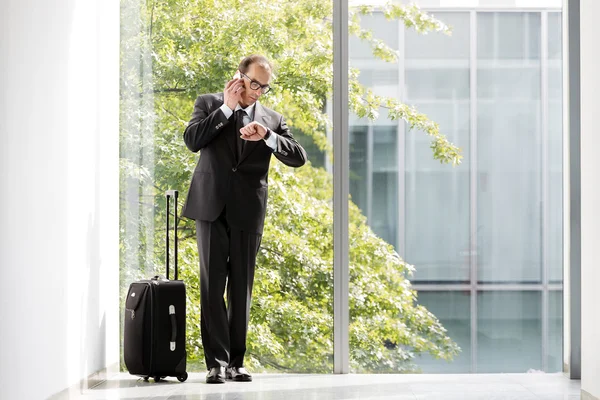 Empresario con maleta mirando su reloj y hablando o — Foto de Stock