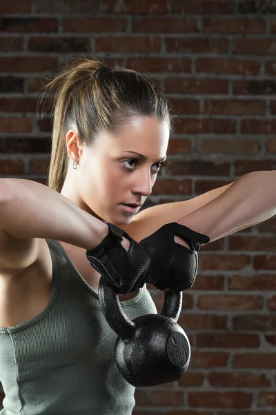 Young fit woman lifting kettle bell on brick background — Stock Photo, Image