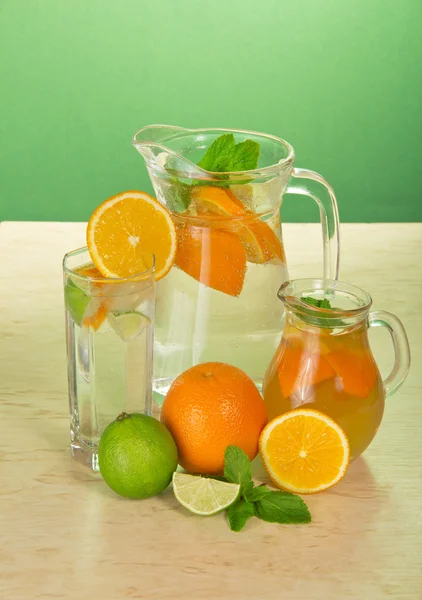 Des cruches avec des boissons, un verre, une lime juteuse et des oranges sur une table — Photo
