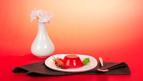 Plate with jelly, a spoon, a vase with the flowers and a brown, napkin on a pink background — Stock Photo, Image