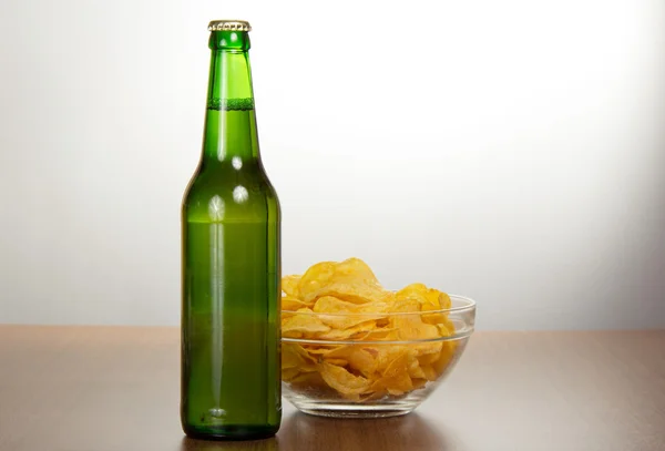 Bottle of beer and bowl with chips on a gray background — Stock Photo, Image