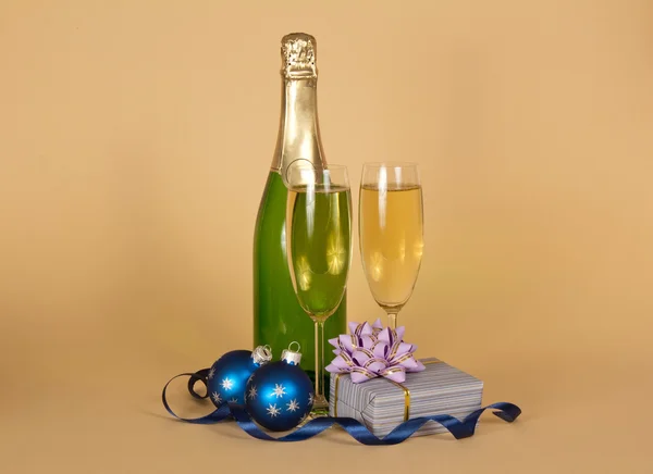 Fles en wijn glazen met champagne, een doos van de gift met een boog, Kerstmis speelgoed en een serpentine op een beige achtergrond — Stockfoto