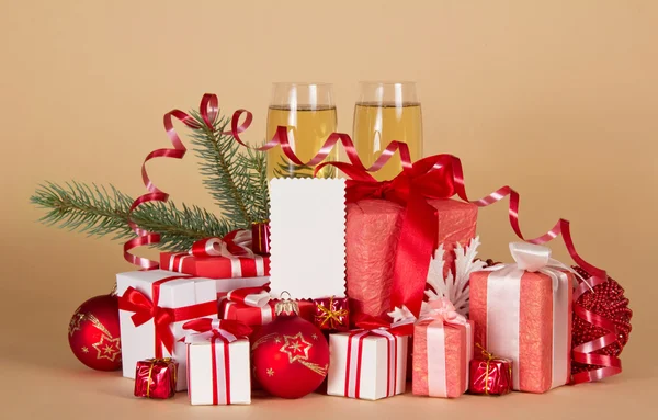 Christmas gifts and toys, pine branch with a serpentine, champagne and an empty card on a beige background — Stock Photo, Image