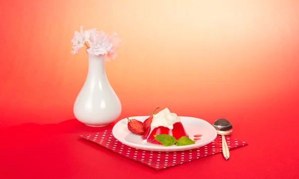 Blommor i en vas, en tallrik med gelé och grädde, en sked och en servett på rosa — Stockfoto