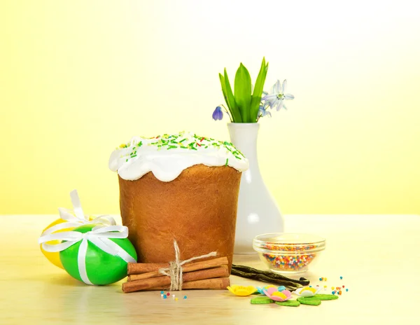 Easter cake, eggs, spices, a vase with the flowers on a table, on a yellow background — Stock Photo, Image