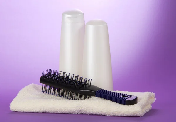 Hairbrush on a towel, shampoo and gel on a violet background — Stock Photo, Image