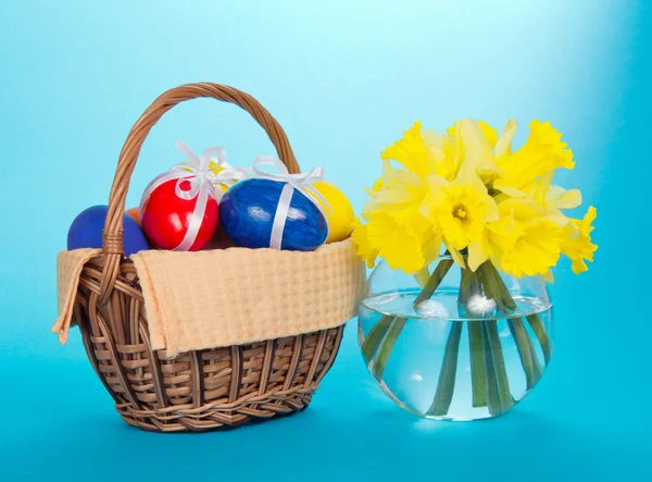 Huevos de Pascua en una cesta con una servilleta y un jarrón con narcisos, en el azul —  Fotos de Stock