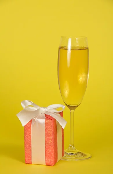 Wine glass with champagne, a gift box with a ribbon and a bow on a yellow background Stock Image