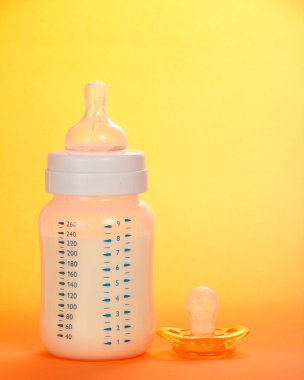 Çocuk küçük şişe süt ve turuncu bir arka plan üzerinde bir emzik