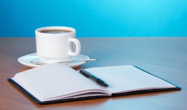 Open Kladblok de greep een kopje koffie in een schotel en een lepel op een tafel