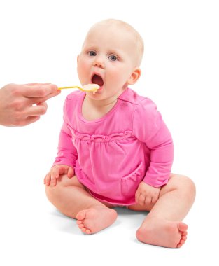 Tatlı küçük bebek kız pembe elbise giymiş bir kaşık beyaz izole yiyor.