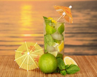 Mojito with umbrellas, a juicy lime, a lemon on a bamboo cloth against the sunset