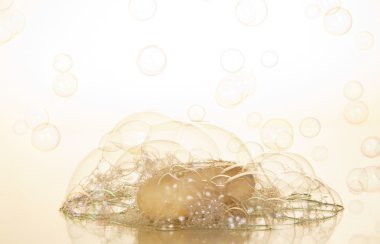 Transparent soap bubbles and piece of soap on a beige background clipart