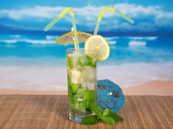 Fresh mojito, umbrella and spearmint leaf on a bamboo cloth, against the sea — Stock Photo, Image