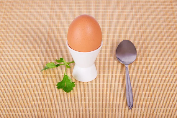 Поддержка с яйцом, стебель петрушки и чайная ложка на бежевом фоне — стоковое фото