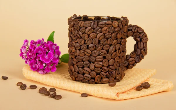 The cup made of grains of coffee, bright carnations, and napkin on the beige — Stock Photo, Image