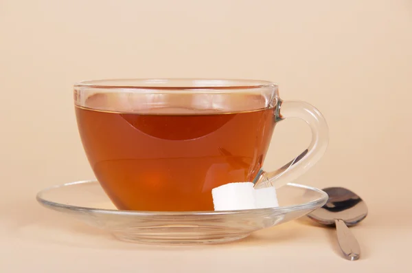 Transparente Tasse mit Tee, Untertasse und Löffel auf beigem Hintergrund — Stockfoto