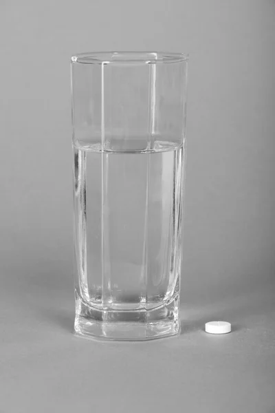 Медицинские таблетки и стекло с водой на сером — стоковое фото