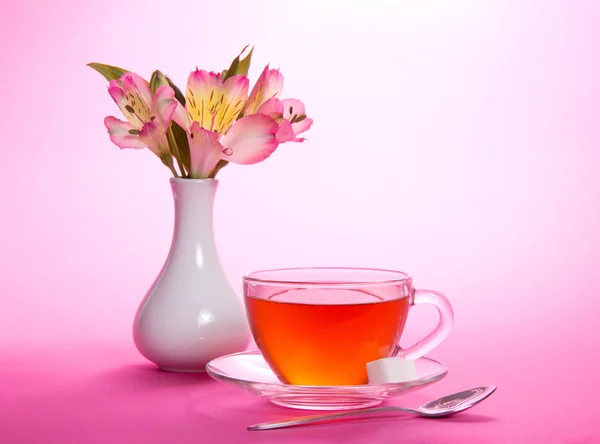 Tazza di tè e zucchero su un piattino, un cucchiaino, vaso con i fiori, su uno sfondo rosa — Foto Stock
