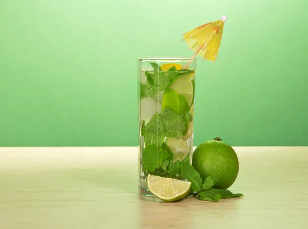 Mojito glass, an umbrella, a leaf of mint and a juicy lime on a table — Stock Photo, Image