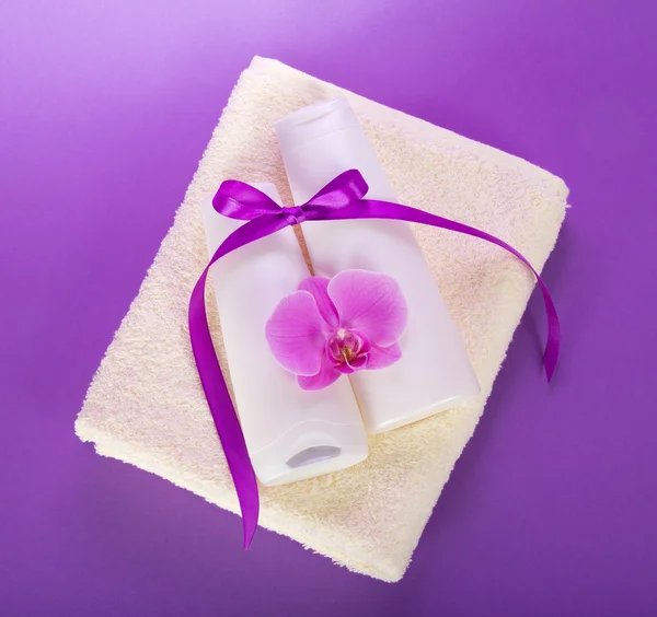 Shampooing et après-shampooing sur une serviette éponge, avec une fleur d'orchidée et un ruban sur la violette — Photo