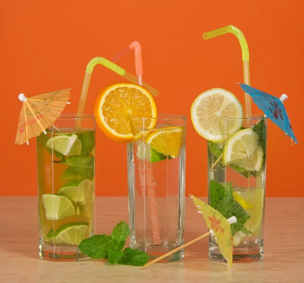 Cóctel con una pajita y un paraguas, bebida con una rebanada de naranja, té con un limón, sobre una mesa — Foto de Stock