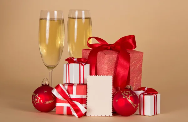 Винні келихи з шампанським, різдвяні подарунки та іграшки та порожня листівка для повідомлень на бежевому фоні — стокове фото