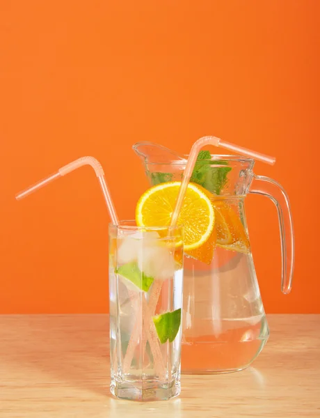 Pot avec boisson, un verre avec paille et une tranche d'orange, sur une table — Photo