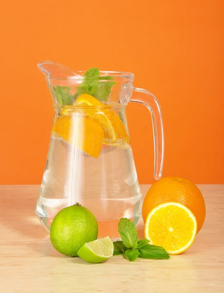 Jug with drink, orange and a juicy lime on a table — Stock Photo, Image
