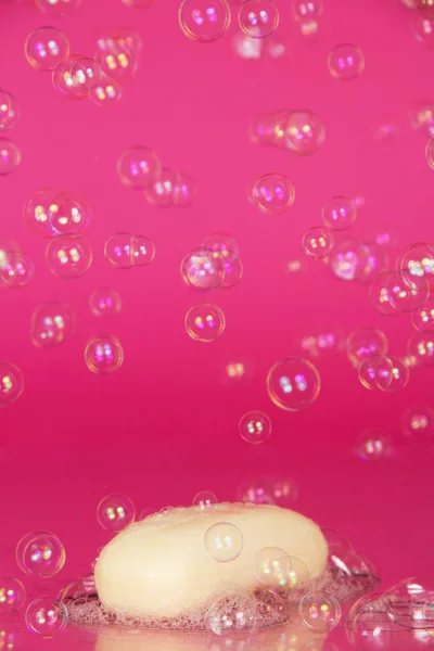 Piece of toilet soap and soapsuds with air bubbles texture, on a pink background — Stock Photo, Image