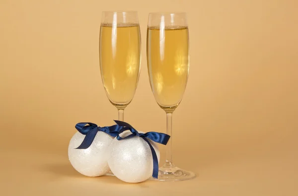 Wine glasses with champagne and New Year's spheres with bows on a beige backgroun — Stock Photo, Image