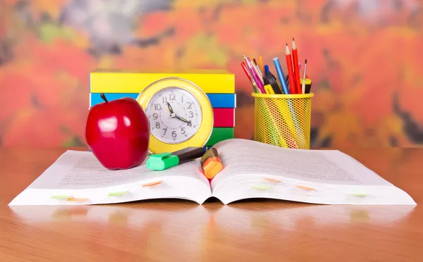 Das aufgeschlagene Buch, ein großer roter Apfel, ein Wecker und Schulzubehör auf einem Tisch — Stockfoto