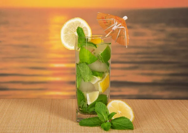 Kald drikke med sitronskive, grønnmynte, på en bambusklut mot solnedgangen – stockfoto